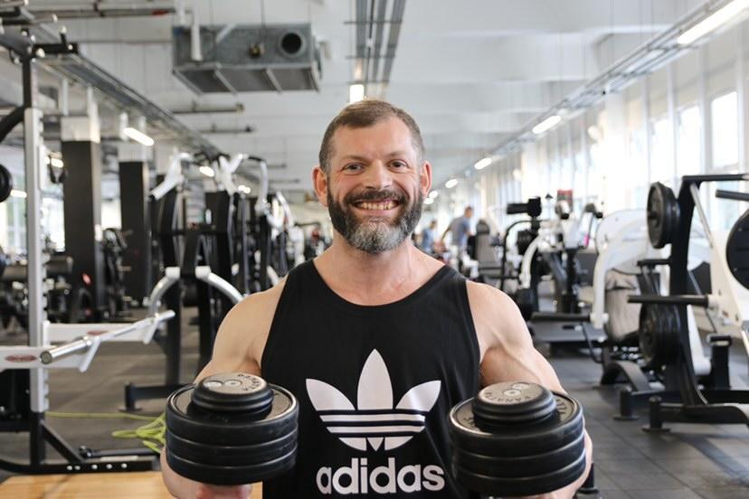 Rich smiling in the gym, holding two dumbbells